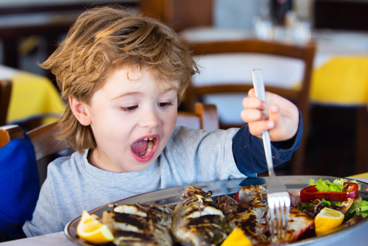 Excited child eats sea fish in a restaurant. Mediterranean diet.